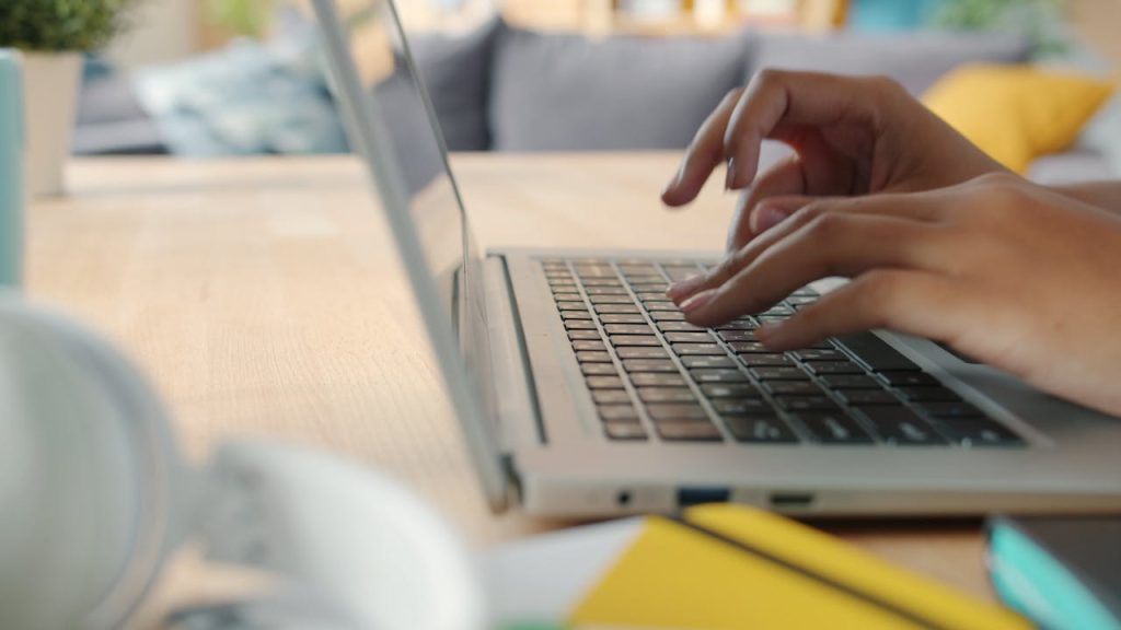 Tarifs Hands typing on a laptop keyboard indoors with blurred background and natural lighting.