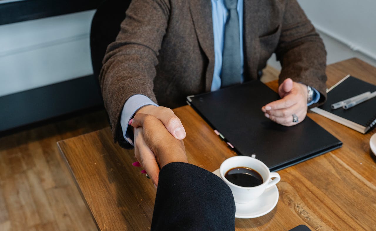 Crop faceless multiracial coworkers in formal clothes sitting at wooden table and shaking hands after successful project