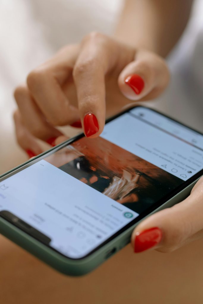 pexels photo 6963589 6963589 A woman with red nails using a smartphone, navigating a social media app.